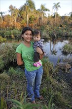 Young mother holding a child in her arms in front of a pond in the community of Mbya-Guarani Indians