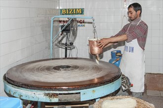 Artisan pouring a continuous stream of highly-fluid dough on a hot plate to prepare the Tel Kadayif or Angels hair