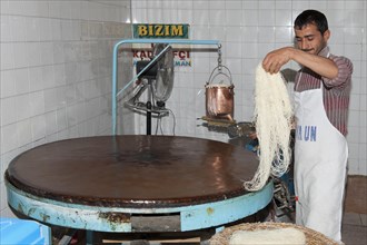 Artisan pouring a continuous stream of highly-fluid dough on a hot plate to prepare the Tel Kadayif or Angels hair