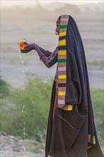Ahir woman in traditional colorful clothes pouring water at sunet