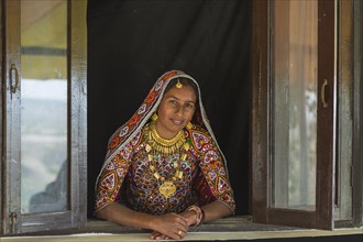 Ahir woman in traditional colorful clothes looking out of a window