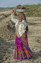 Fakirani woman in traditional colorful clothes carrying earth on her head for road works