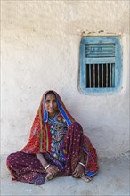 Woman in traditional colorful clothes sitting against a wall