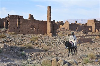 Rider on a donkey in front of dilapidated mud houses