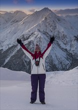 Woman with arms outstretched standing in front of an Alpine panorama