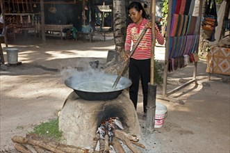 Khmer woman stirring palm sap in a traditional heated metal boiler to produce palm sugar