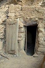 Entrance with a carved wooden door to a stone hut at the abandoned settlement of Sap Bani Khamis under a ledge in the Grand Canyon of Oman in the Wadi at Nakhar