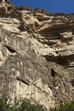 Rock face at the western flank of the Grand Canyon of Oman in the Wadi at Nakhar with hikers on the fixed climbing route leading to the exit from the gorge