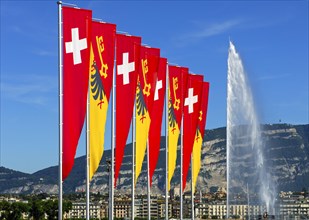 Flags of the Swiss Confederation and the Canton of Geneva on the promenade of Lake Geneva with the Jet d'Eau fountain and the summit of Saleve Mountain at the rear