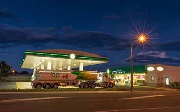Tanker truck in front of petrol station with street lighting at night