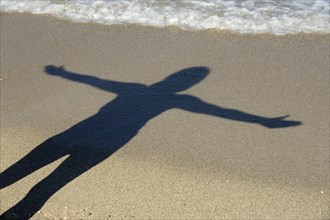 Woman with outstretched arms casting her shadow on the beach