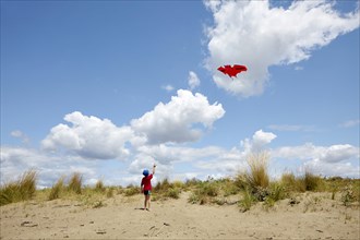 Boy flying a red kite on a dune