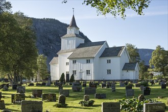 Large white wooden church with a cemetery at the front and a rockface at the rear