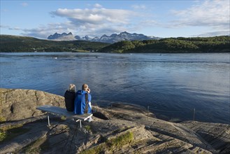 Couple sitting on a bench looking out to the tidal Saltstraumen strait in the evening light