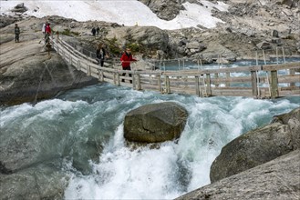 Hikers crossing a hanging bridge over a glacial river