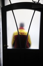 DHL parcels delivery driver is standing in front of a front door with frosted glass