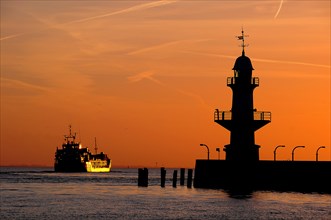 Cargo ship and silhouette of the Brunsbuttel Mole 1 lighthouse in front of a evening sky