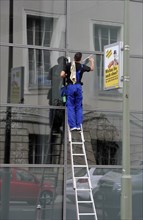 Window cleaner standing on a ladder cleaning a glass facade