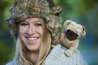 Young woman wearing a fur hat with a plush pug on her shoulder