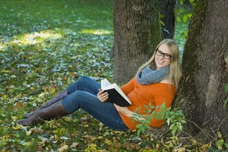Young woman wearing glasses sitting in the park and reading a book