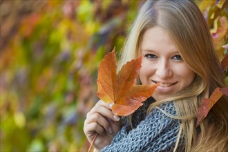 Young woman wearing a thick scarf and holding an autumnal coloured leaf in her hand