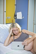 Pregnant woman lying in the delivery room on the delivery bed and looking at a tablet PC