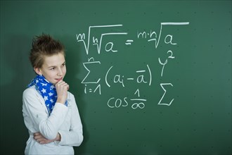 Schoolboy pondering a mathematical formula on a school blackboard