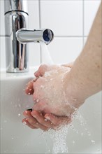 Person washing their hands under running water from a faucet