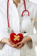 Female doctor holding a red heart with a plaster in her hands