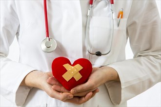 Female doctor holding a red heart with a plaster in her hands