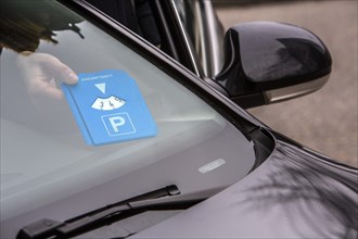 Woman putting a parking disc with her arrival time behind the windscreen