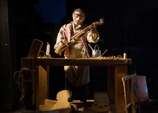 Violin maker as wooden figure at work in violin making workshop