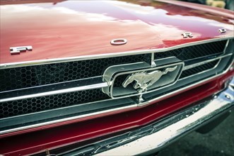 Ford logo and Mustang emblem on the radiator grille of a red 1965 First Generation Ford Mustang Coupe