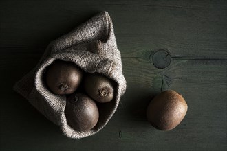 Kiwi fruits in jute sack lying on a wooden table