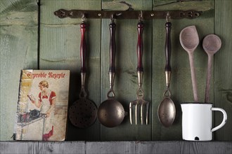 Old cookbook and cooking utensils in front of a green wooden wall