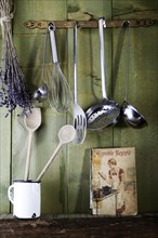 Old cookbook with cooking utensils in front of a green wooden wall