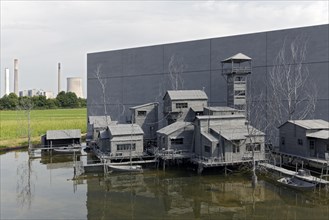 Village on stilts in front of an industrial scene