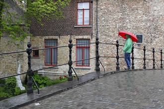 Woman with red umbrella in rain on bridge at Begijnhof nunnery