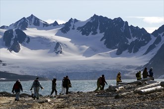 Expedition participants hiking near Smeerenburg in front of the mountain and glacier scenery of Vasahalvoya