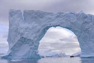 Zodiac inflatable boat seen through the arch of a large iceberg