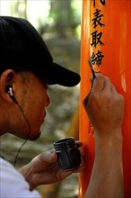 Man writing the name of donors with a brush on to a Torii