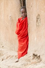 Maasai child wearing traditional dress looking out of a mud hut