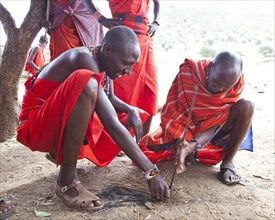 Maasai warriors wearing traditional dress starting a fire with a fire stick