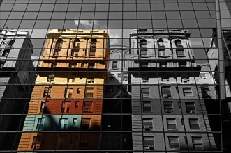 Houses are reflected in the glass facade of a skyscraper