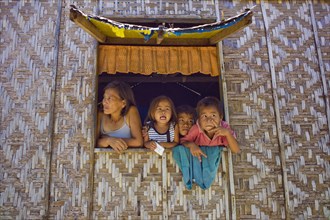 Filipino mother and children looking out of a window of their home