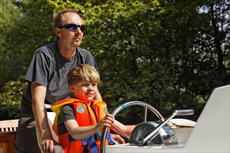 Father and son at the helm of a houseboat on the Canal du Midi near Bram