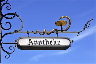 Hanging sign of St. George Apotheke pharmacy against a blue sky