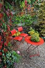 Red garden chairs and table in the rain in an autumn garden corner