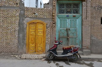 Motor scooter in front of old Uighur Muslim doorframes in new homes