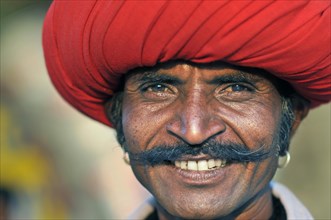Man wearing a red turban with a moustache and a blue shirt